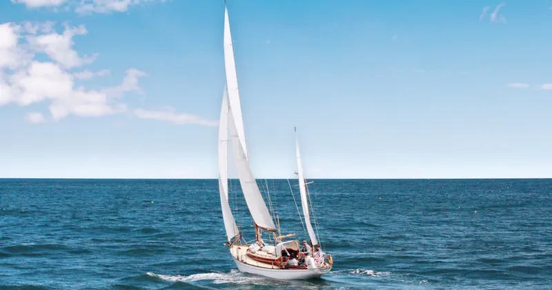 White catamaran sailing along the Ibiza coastline with passengers relaxing on the foredeck nets