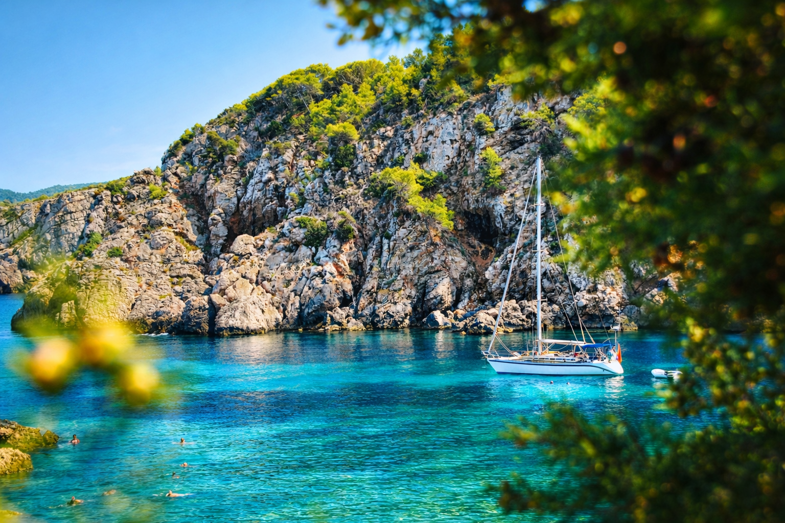 Sailboat anchored in a calm turquoise cove in Ibiza framed by rocky cliffs and pine trees