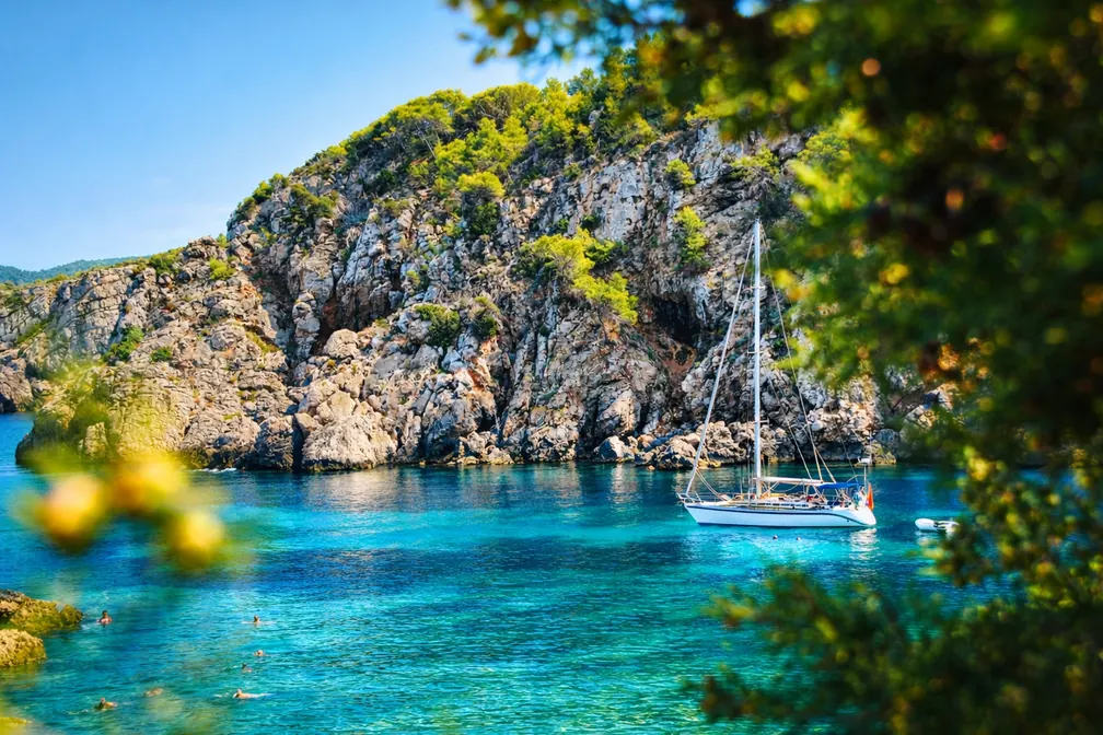 Velero fondeado en una cala turquesa y tranquila de Ibiza entre acantilados y pinos