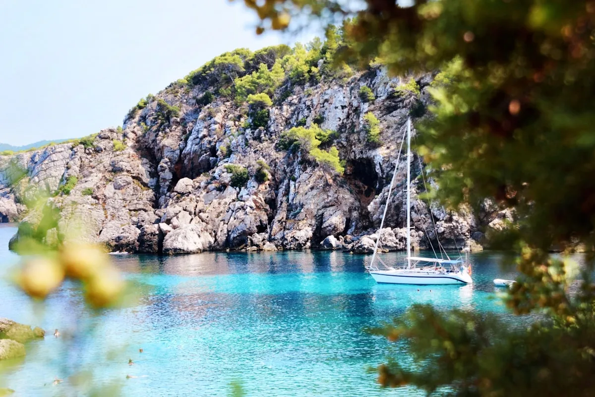 Dramatic cliff cove with a boat anchored in turquoise water, pine trees above